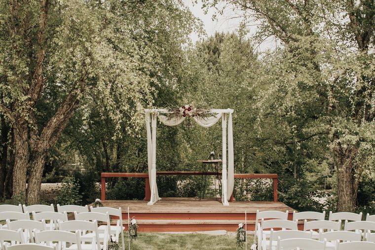Wooden ceremony arch and white chairs ready on the lawn at On Collin's Pond in Middleton, Idaho