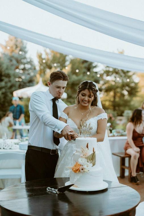 Couple cutting their wedding cake under the canopy at On Collin's Pond