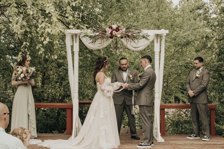 Bride and groom exchanging vows at the floral arch at On Collin's Pond