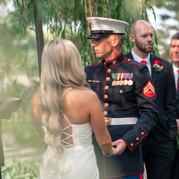 Bride and Marine groom holding hands during their ceremony at On Collin's Pond