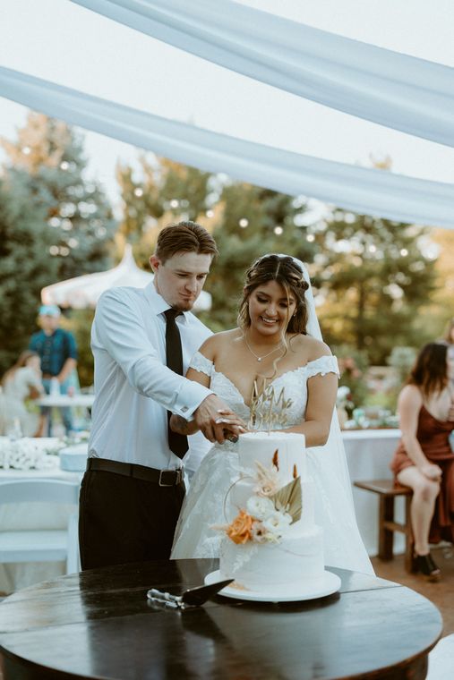 Couple serving cake beneath the reception canopy at On Collin's Pond