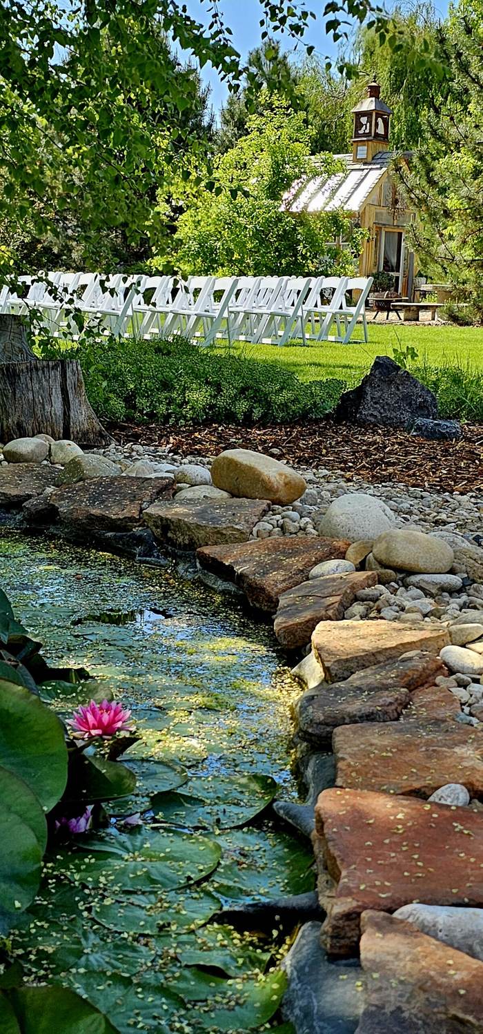 Stone stream flowing into the koi pond with the old-world greenhouse behind at On Collin's Pond garden venue in Middleton, Idaho