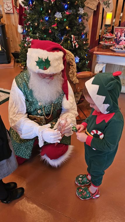 Santa Phil and an elf greeting a young visitor in the lodge at On Collin's Pond