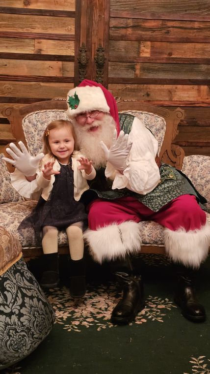 A little girl waving beside Santa Phil on the settee at On Collin's Pond