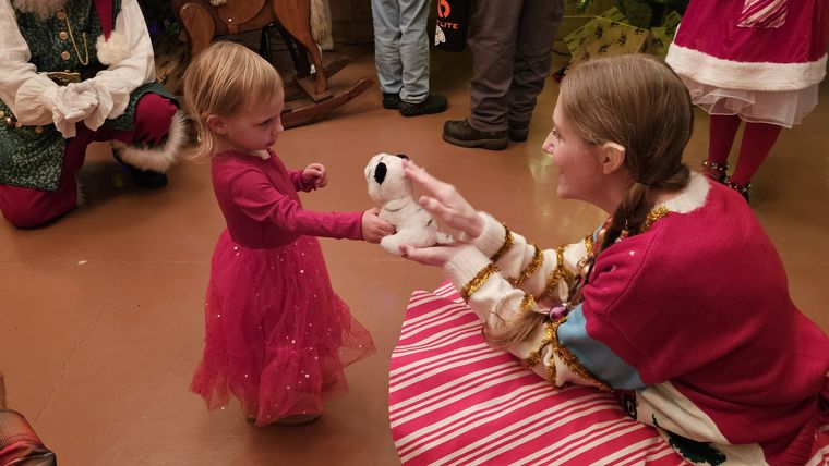 An elf showing a small visitor a toy in the lodge at On Collin's Pond