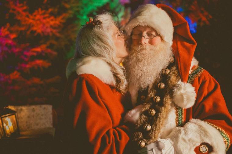 Mrs. Claus kissing Santa's cheek amid the coloured Christmas lights, photographed by Jerry Moyer Photography