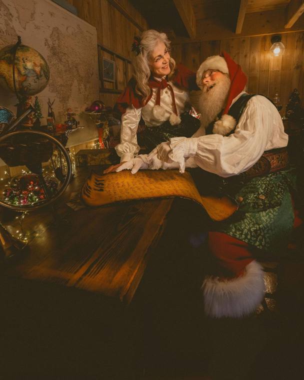 Santa and Mrs. Claus reviewing the list together by lamplight in the workshop, photographed by Jerry Moyer Photography
