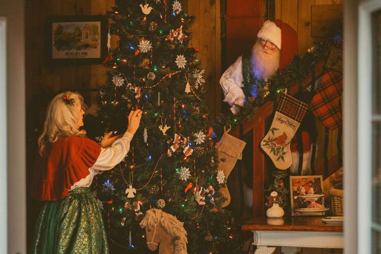 Mrs. Claus trimming the Christmas tree while Santa looks on, photographed by Jerry Moyer Photography