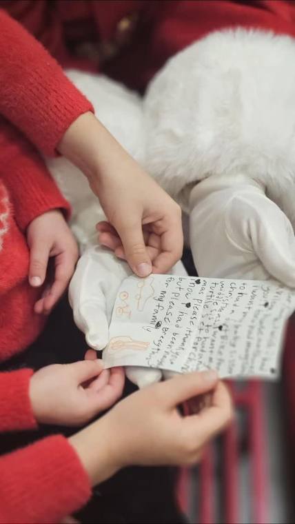 A child's hands unfolding a handwritten letter to Santa at the Kids' Workshop