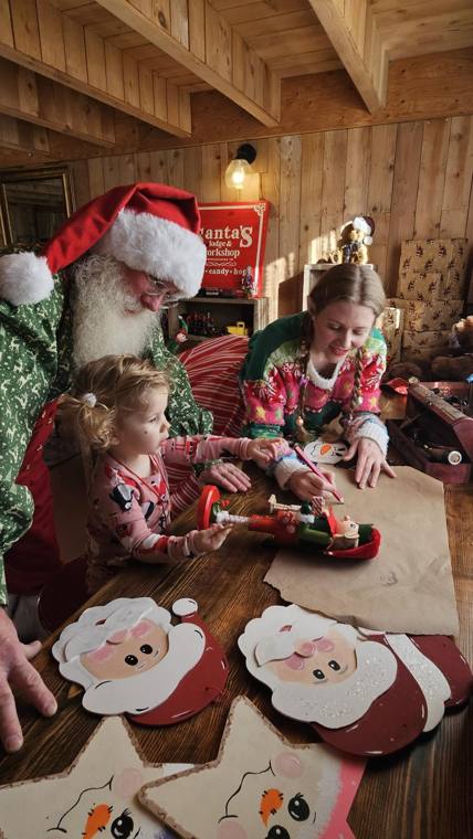 Santa and an elf helping a small child with crafts at Santa's Lodge and Workshop