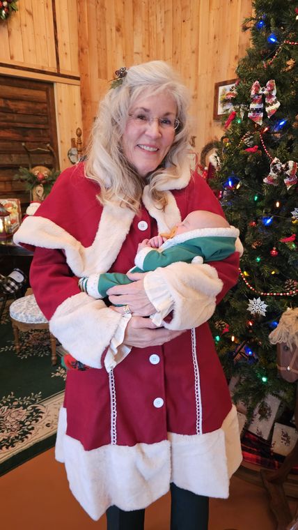 Mrs. Claus holding a baby beside the Christmas tree at Santa's Workshop on Collin's Pond