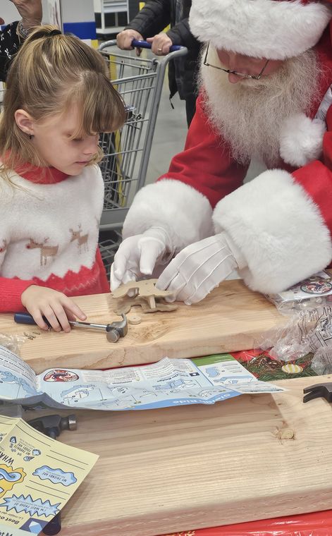 Santa Phil helping a girl with a Christmas craft at an off-site event