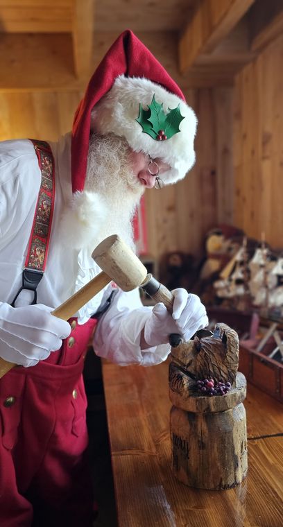 Santa Phil carving a wooden toy at the workbench in Santa's Lodge and Workshop