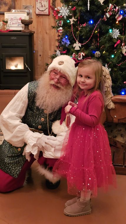 Santa Phil greeting a little girl by the Christmas tree at On Collin's Pond