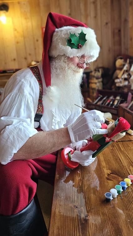 Santa Phil hand-painting a wooden toy at his workbench in the workshop