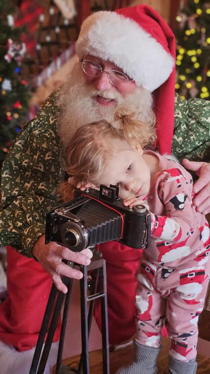 Santa Phil showing a toddler the antique camera in the workshop at On Collin's Pond