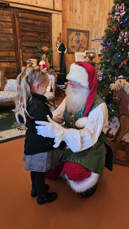 Santa Phil kneeling to greet a young visitor in the lodge at On Collin's Pond