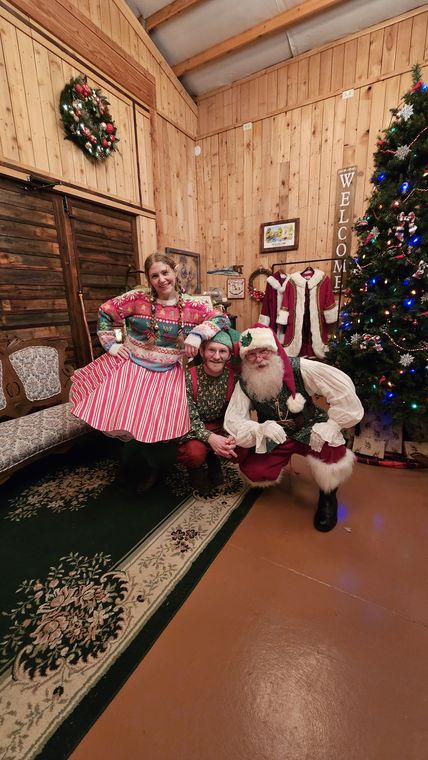 Santa Phil and an elf by the Christmas tree in the lodge at On Collin's Pond
